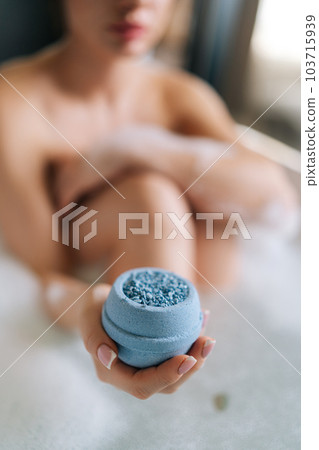 Closeup vertical cropped shot of unrecognizable young woman sitting in foam holding bath bomb above water. Soap ball dissolving, foam bubbles. Concept of decorative cosmetic products for bathroom. Closeup vertical cropped shot of unrecognizable young woman sitting in foam holding bath bomb above water. Soap ball dissolving, foam bubbles. Concept of decorative cosmetic products for bathroom. 103715939