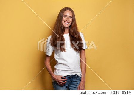 Cheerful mid adult woman in white t-shirt against yellow studio wall background 103718519