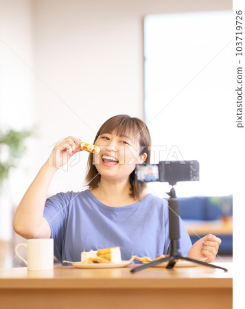 Young woman eating sweets while photographing herself with a camera 103719726