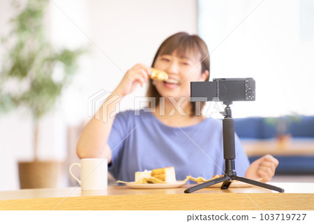 Young woman eating sweets while photographing herself with a camera 103719727