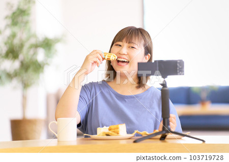Young woman eating sweets while photographing herself with a camera 103719728
