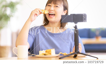 Young woman eating sweets while photographing herself with a camera 103719729