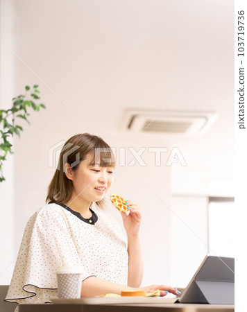A young woman working on a computer while eating waffles A young woman working on a computer while eating waffles 103719736