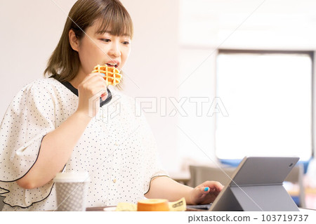 Young woman looking at tablet screen while eating waffles Young woman looking at tablet screen while eating waffles 103719737