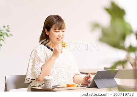 Young woman looking at tablet screen while eating waffles Young woman looking at tablet screen while eating waffles 103719738
