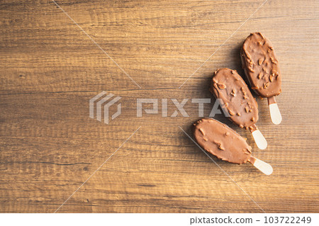 Popsicle, ice cream covered with chocolate on wooden table. Top view. Popsicle, ice cream covered with chocolate on wooden table. Top view. 103722249