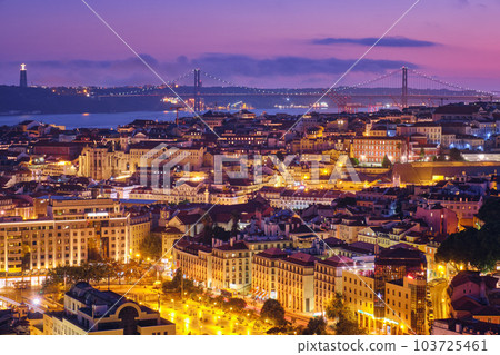 Night view of Lisbon famous view from Miradouro da Senhora do Monte tourist viewpoint of Alfama and Mauraria old city districts, 25th of April Bridge in the evening twilight. Lisbon, Portugal 103725461