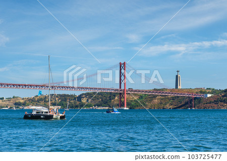 View of 25 de Abril Bridge famous tourist landmark over Tagus river, Christ the King monument and a tourist yacht boat. Lisbon, Portugal View of 25 de Abril Bridge famous tourist landmark over Tagus river, Christ the King monument and a tourist yacht boat. Lisbon, Portugal 103725477