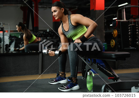 Young woman working out with dumbbell in modern gym 103726015