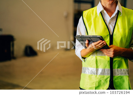 Warehouse engineer with safety vest using tablet for checking goods on shelves 103726194