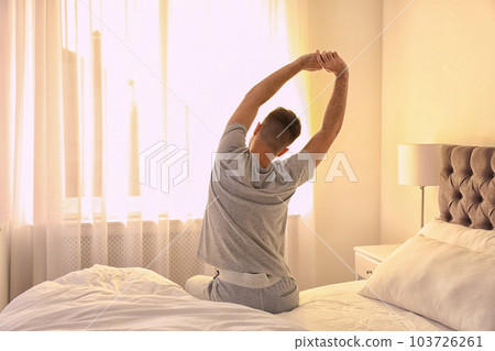 Young man stretching on bed at home, view from back. Lazy morning 103726261