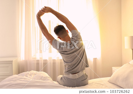 Young man stretching on bed at home, view from back. Lazy morning Young man stretching on bed at home, view from back. Lazy morning 103726262