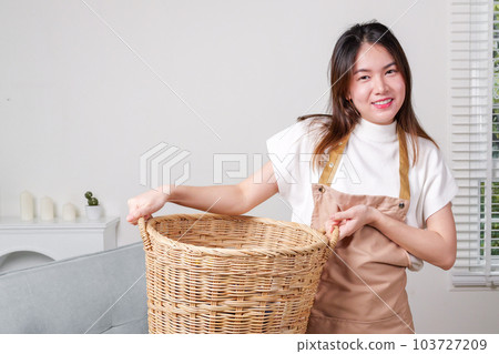 Female housekeeper cleaner taking messy dirty clothes on sofa into basket Female housekeeper cleaner taking messy dirty clothes on sofa into basket 103727209