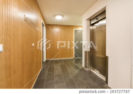 a long hallway with wood walls and tile flooring on both sides, leading to an elevator in the center a long hallway with wood walls and tile flooring on both sides, leading to an elevator in the center 103727787