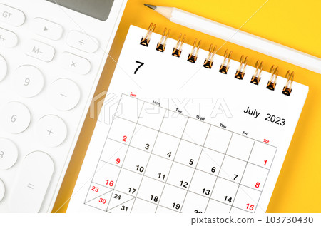 The July 2023 Monthly desk calendar for 2023 year and calculator with pen on yellow background. 103730430