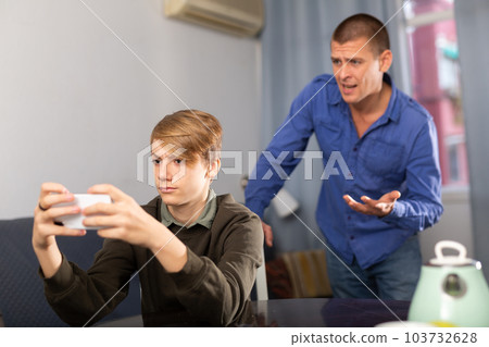 Boy sitting with phone and playing, ignoring his father Boy sitting with phone and playing, ignoring his father 103732628