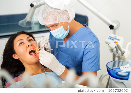 Man dentist examines a female patient with the help of working tools 103732692