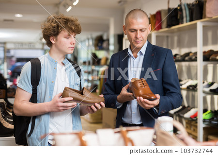 Shoe store employee helping teen to choose classic brown shoes in shoe store Shoe store employee helping teen to choose classic brown shoes in shoe store 103732744