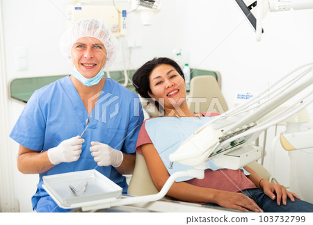 Portrait of a smiling man dentist with a positive woman patient sitting in a dental chair Portrait of a smiling man dentist with a positive woman patient sitting in a dental chair 103732799