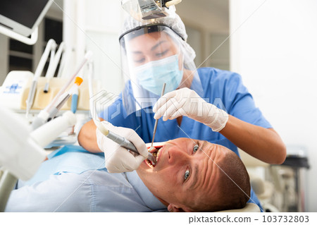 Female dentist drilling tooth to male patient 103732803