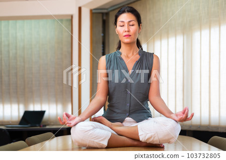 Businesswoman sitting at the table in lotus position Businesswoman sitting at the table in lotus position 103732805
