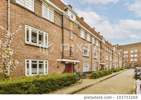 a bricked street with cars parked on the side and trees in blooming bushes growing along the curbs a bricked street with cars parked on the side and trees in blooming bushes growing along the curbs 103733269