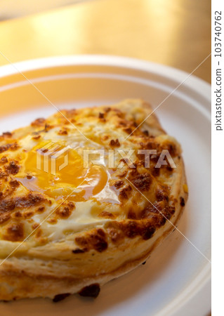 Traditional Georgian cuisine. Ajara khachapuri on paper plate. Filled with cheese and topped with raw egg and butter, cheese-filled bread Traditional Georgian cuisine. Ajara khachapuri on paper plate. Filled with cheese and topped with raw egg and butter, cheese-filled bread 103740762