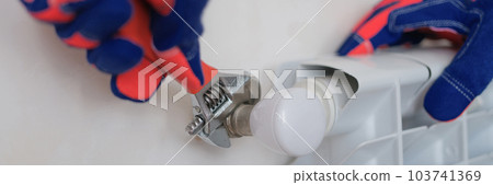 Plumber hands in protective gloves installing heating radiator Plumber hands in protective gloves installing heating radiator 103741369