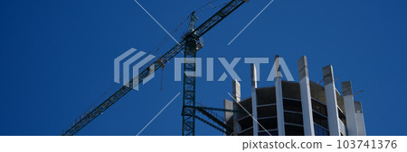 Tower crane in action construction of a new round shaped multi-storey building 103741376