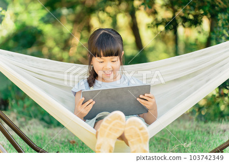 A child watching a video on a hammock at an outdoor campsite (outside play) 103742349