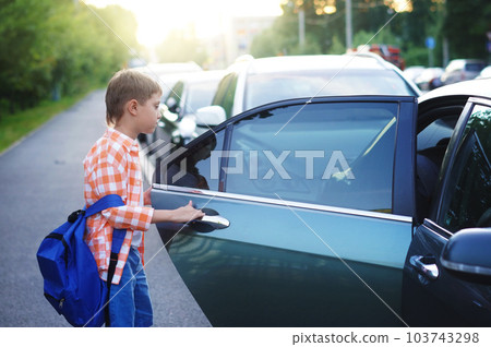 caucasian boy getting in car returning from school wearing school bag. caucasian boy getting in car returning from school wearing school bag. 103743298
