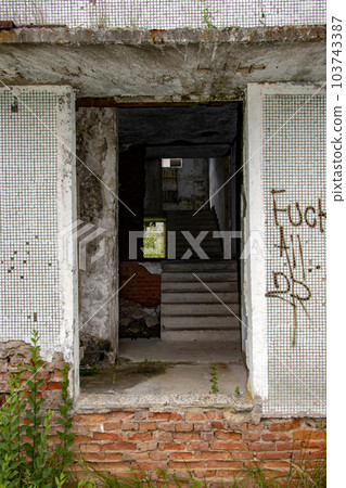 A damaged entrance at a abandoned panel house with decorative facade of small white tiles. A damaged entrance at a abandoned panel house with decorative facade of small white tiles. 103743387