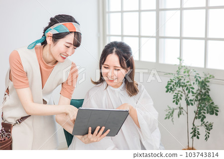 A hairdresser counseling a customer woman who uses a tablet to consult a hair style / hair style at a beauty salon / hair salon A hairdresser counseling a customer woman who uses a tablet to consult a hair style / hair style at a beauty salon / hair salon 103743814