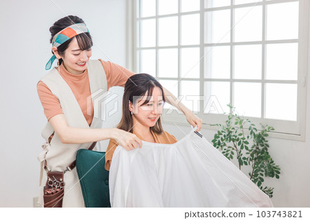 Hairdresser / barber Asian woman wearing a cross cape to a customer who came to a beauty salon / hair salon 103743821