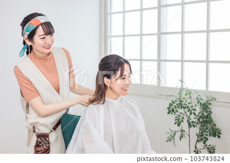 美髮師/理髮師亞洲女性穿著十字斗篷給來美容院/美髮沙龍的顧客 美髮師/理髮師亞洲女性穿著十字斗篷給來美容院/美髮沙龍的顧客 103743824