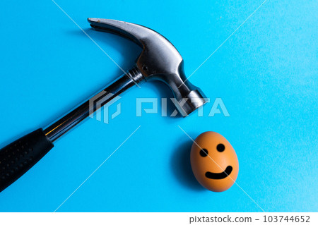 Hammer is hitting on an egg with blue background. minimal idea creative concept. Hammer is hitting on an egg with blue background. minimal idea creative concept. 103744652