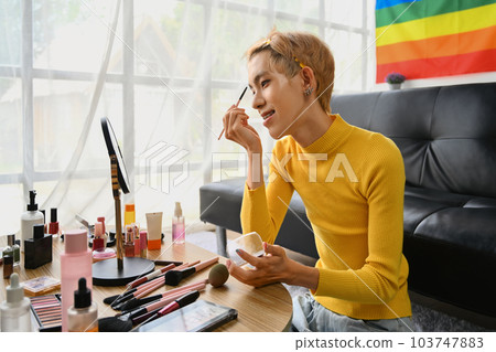 Smiling Asian gay man blogger filming daily makeup routine tutorial on smartphone. LGBTQ, domestic life and beauty concept 103747883