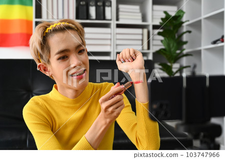 Smiling Asian gay man blogger filming daily makeup routine tutorial on smartphone. LGBTQ, domestic life and beauty concept Smiling Asian gay man blogger filming daily makeup routine tutorial on smartphone. LGBTQ, domestic life and beauty concept 103747966
