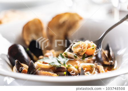 Shrimp on a spoon taken out of a seafood soup in a plate 103748508