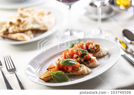 Italian appetizer with three bruschettas topped with tomatoes and greens in a cafeteria Italian appetizer with three bruschettas topped with tomatoes and greens in a cafeteria 103748509