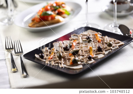 Italian appetizer with veal slices, tuna salsa and olives served in an Italian restaurant 103748512