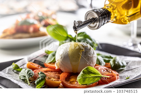 Olive oil poured over buffalo mozzarella ball on a differently styled Caprese salad Olive oil poured over buffalo mozzarella ball on a differently styled Caprese salad 103748515