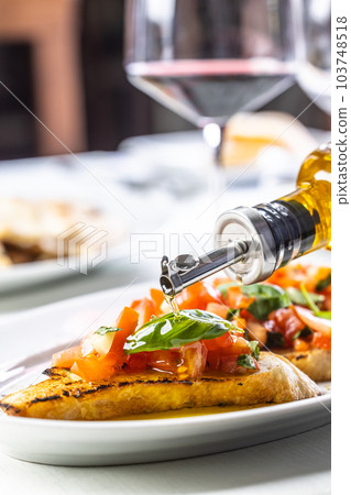 Italian classical bruschetta gets olive oil drizzle with red wine glass in the background 103748518