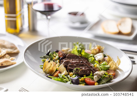 Beef steak sliced on top of mixed salad with greens, physalis, cherry tomatoes served with wine 103748541