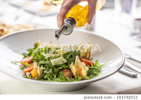 Olive oil pouring over a fresh rocket salad with parmesan shavings and physalis Olive oil pouring over a fresh rocket salad with parmesan shavings and physalis 103748552