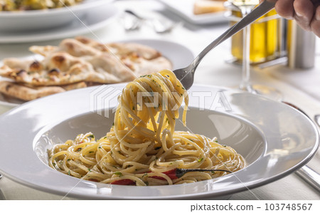 Hand with a fork spinning spaghetti aglio e olio peperoncino from a plate in a restaurant 103748567
