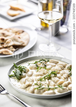 Gnocchi with white cheesy sauce topped with rocket leaves served with white wine 103748589