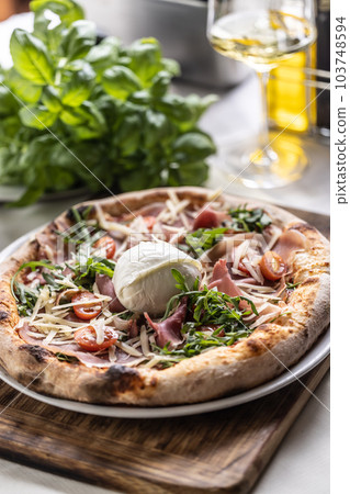 Round buffalo mozzarella on top of a ham, tmatoes and rocket pizza with crusty edges 103748594
