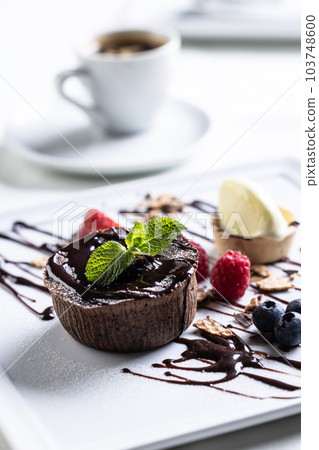 Brownies with ice cream and fruit, mint and chocolate decoration with an espresso on a cafe table Brownies with ice cream and fruit, mint and chocolate decoration with an espresso on a cafe table 103748600