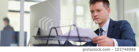Businessman taking out paper from tray on desk in office 103748998